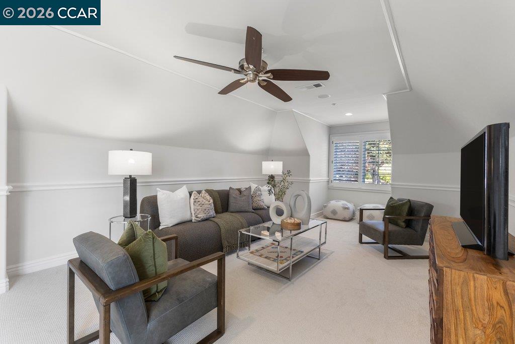 Living room with gray seating, a glass coffee table, ceiling fan, and shuttered windows.