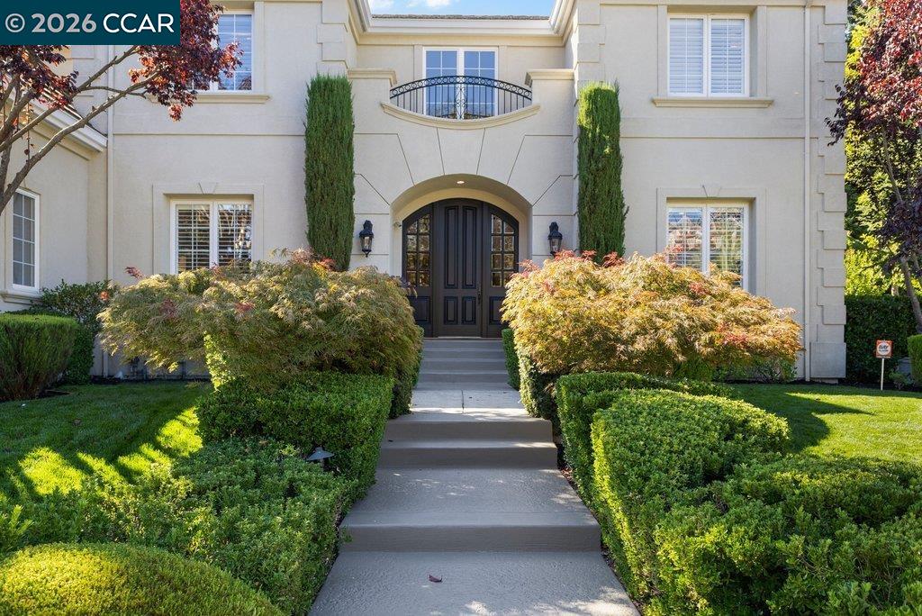 Home entrance with dark double doors, arched portico, and clipped hedges along the walkway.