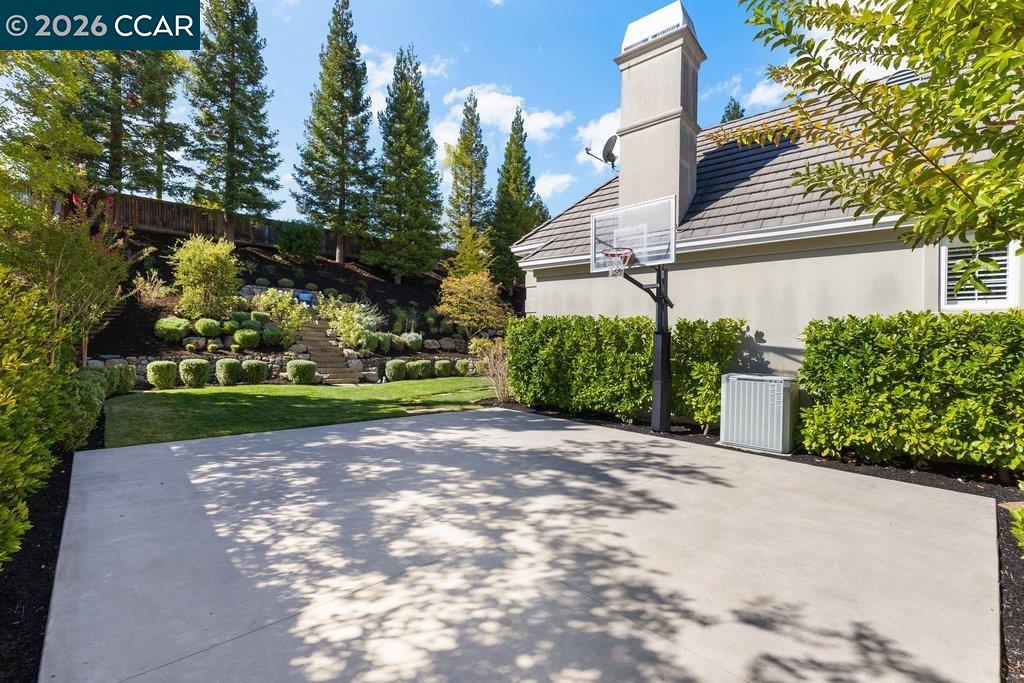 Backyard patio with a basketball hoop, landscaped lawn, and terraced garden beside the house.