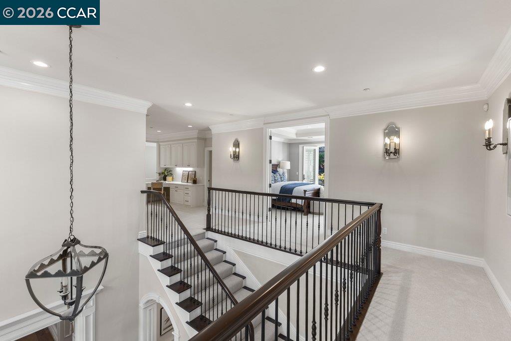 Upper-level landing with a carpeted staircase, dark iron railing, and a bedroom visible through the doorway.