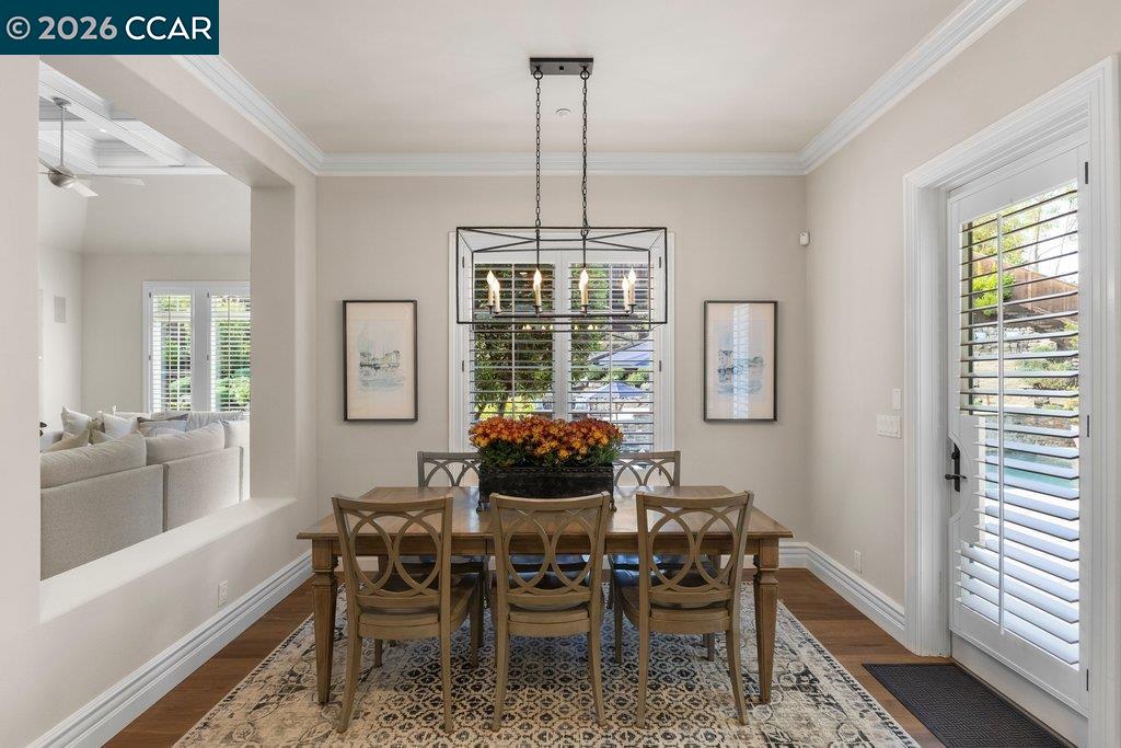 Dining room with a wooden table, six chairs, chandelier, and plantation shutters.
