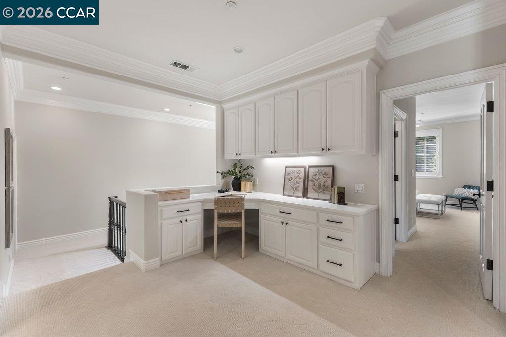 Built-in office with white cabinetry, a desk, and a doorway to a sitting room.