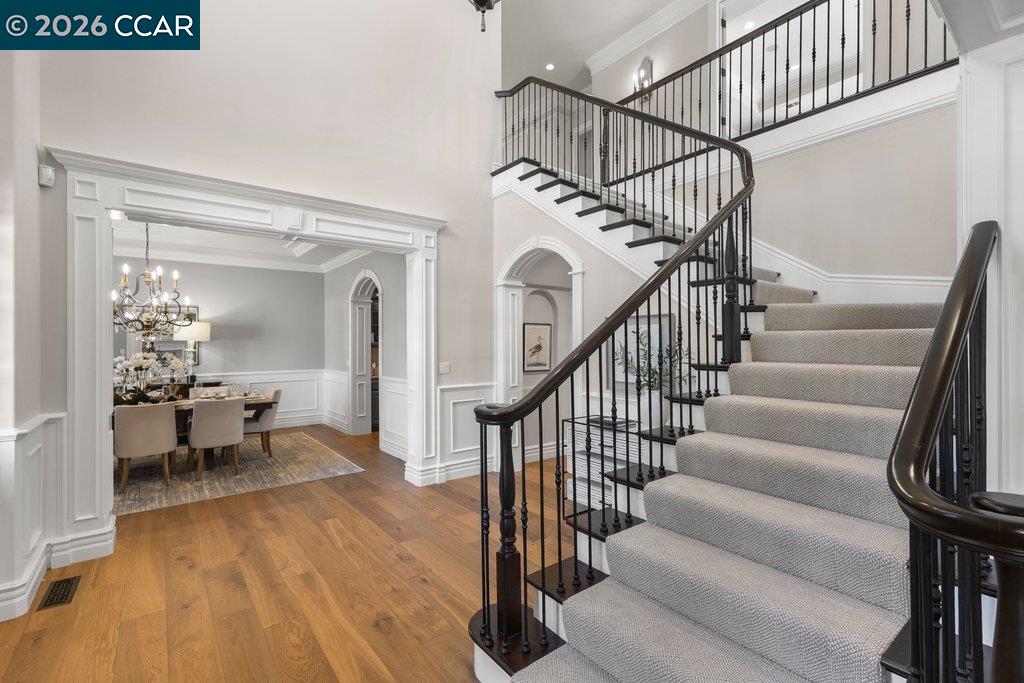 Grand foyer with a carpeted staircase, dark iron railings, and an adjoining dining room.