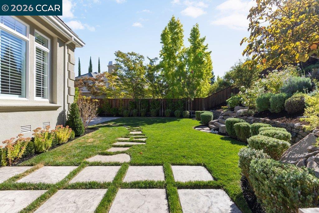 Landscaped backyard with a broad lawn, large stone stepping pads, and a tiered garden beside the house.