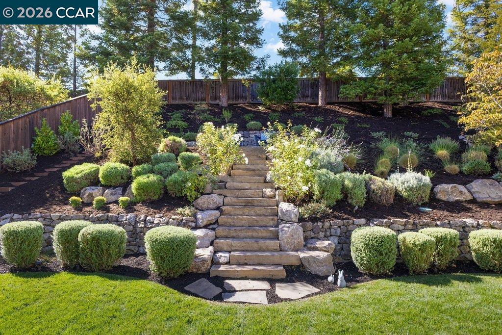 Landscaped backyard with stone steps, terraced planting beds, and a wooden fence.