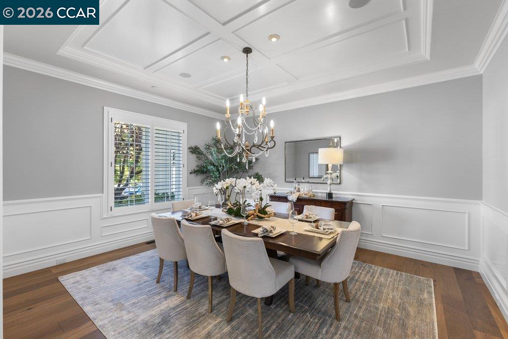 Dining room with a set table, upholstered chairs, and a chandelier beneath a coffered ceiling.