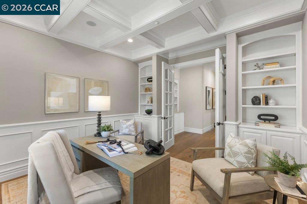 Staged home office with a coffered ceiling, built-in shelving, and a desk beside French doors.