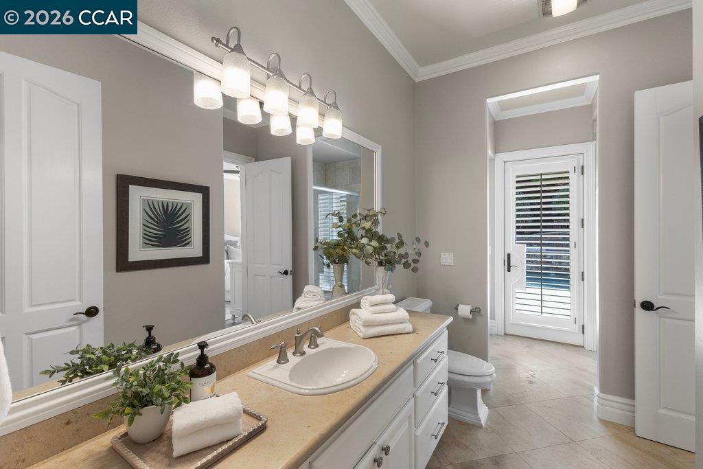 Bathroom with a long double-sink vanity, framed botanical art, and a shuttered glass door.