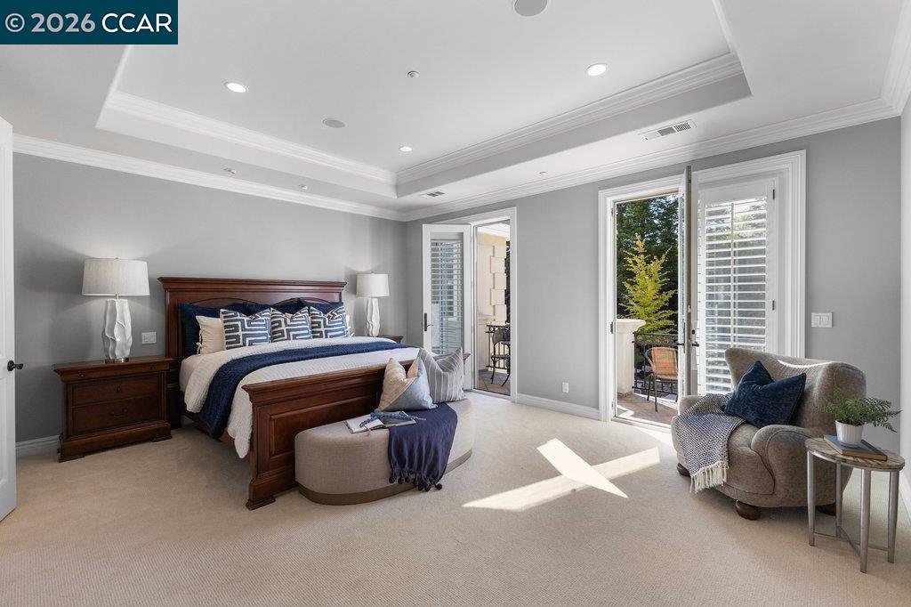 Staged bedroom with a dark wood bed, tray ceiling, and doors opening to a patio.