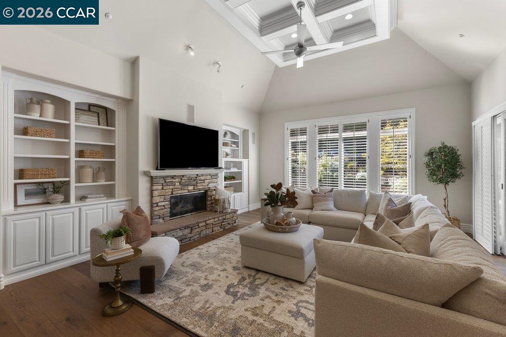 Living room with a stone fireplace, built-in shelving, vaulted ceiling and large shuttered windows.