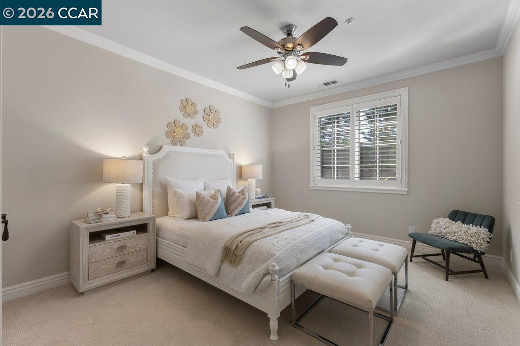 Staged bedroom with a white upholstered bed, tufted bench, and shuttered window.