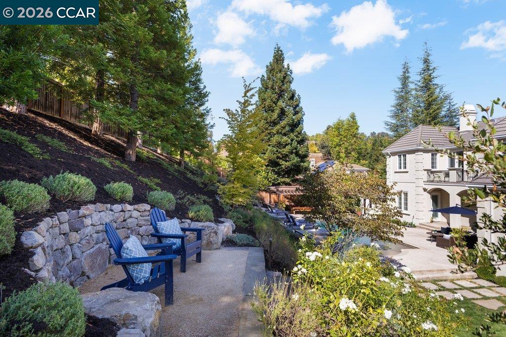 Landscaped backyard patio with blue chairs, a stone retaining wall, and the home beyond.
