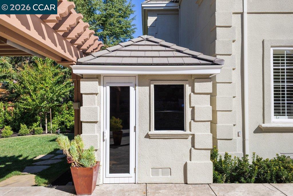 Home exterior with a glass door, tiled awning, pergola, and landscaped patio.