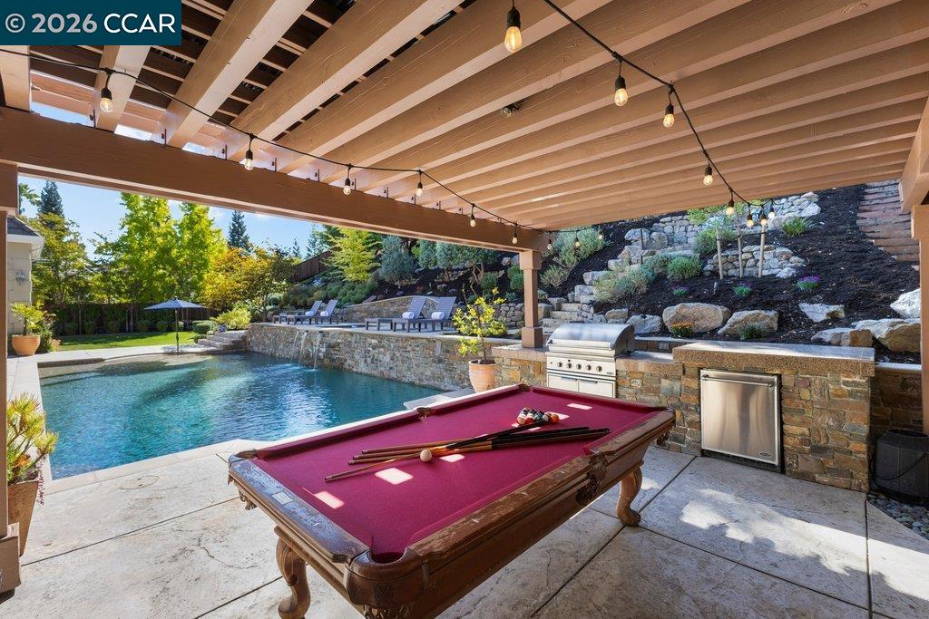 Covered patio with a pool, outdoor kitchen, and red-felt billiards table.
