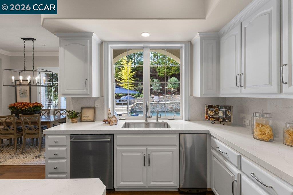 White kitchen with a central sink facing windows overlooking a pool.