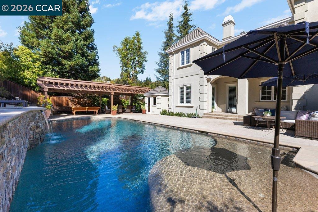 Backyard swimming pool with a shallow tanning ledge, stone waterfall, and shaded patio beside the house.