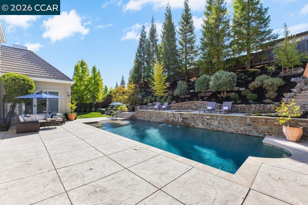 Backyard swimming pool beside a stone retaining wall and landscaped hillside.