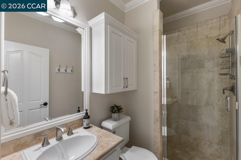 Bathroom with a stone-tile shower, marble-look vanity, and white cabinetry.