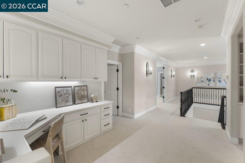 Carpeted upstairs landing with a built-in desk and cabinets beside a black stair railing.