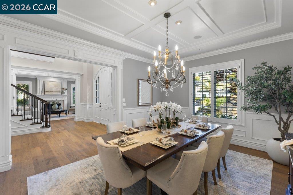 Dining room with a set table beneath a chandelier and coffered ceiling.