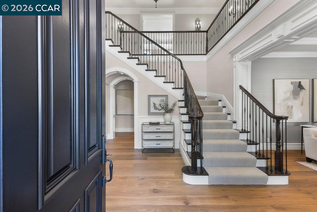 Grand entry foyer with a sweeping carpeted staircase, dark iron railings, and hardwood floors.