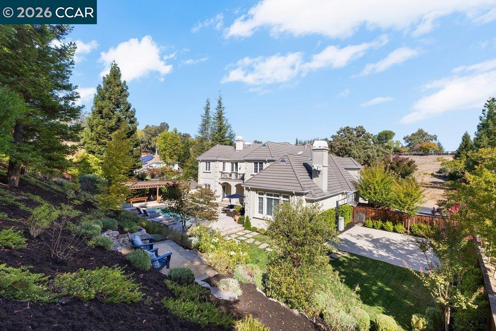 Elevated view of a tiled-roof home surrounded by landscaped grounds, patio seating, and a swimming pool.