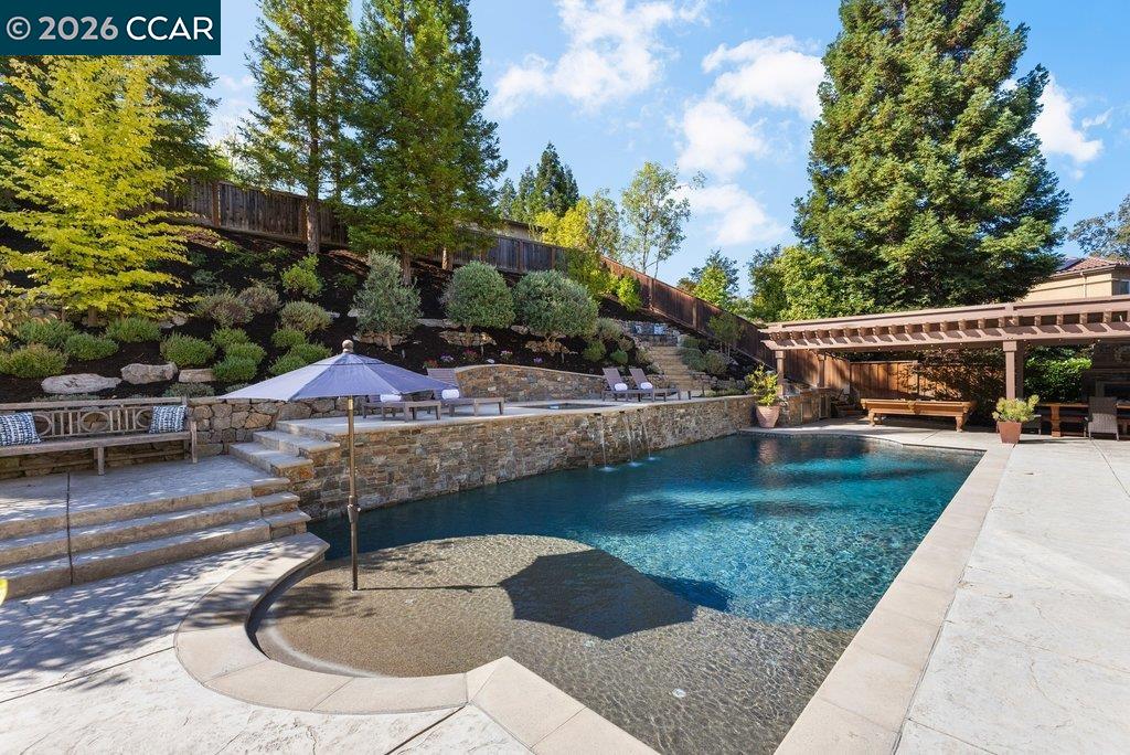 Backyard swimming pool with shallow sun shelf, stone terraces, and a covered patio.