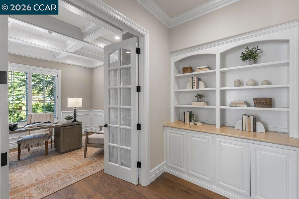 Home office with built-in shelves, a glass-paneled door, and a desk beside shuttered windows.
