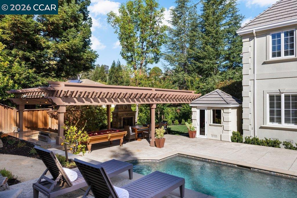 Backyard pool beside a pergola-covered patio with lounge chairs and an outdoor fireplace.
