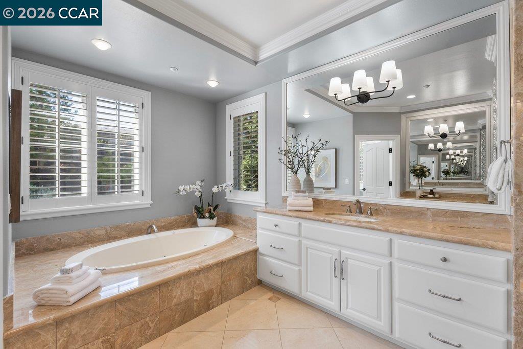 Bathroom with a corner soaking tub, tan stone surround, and white vanity.