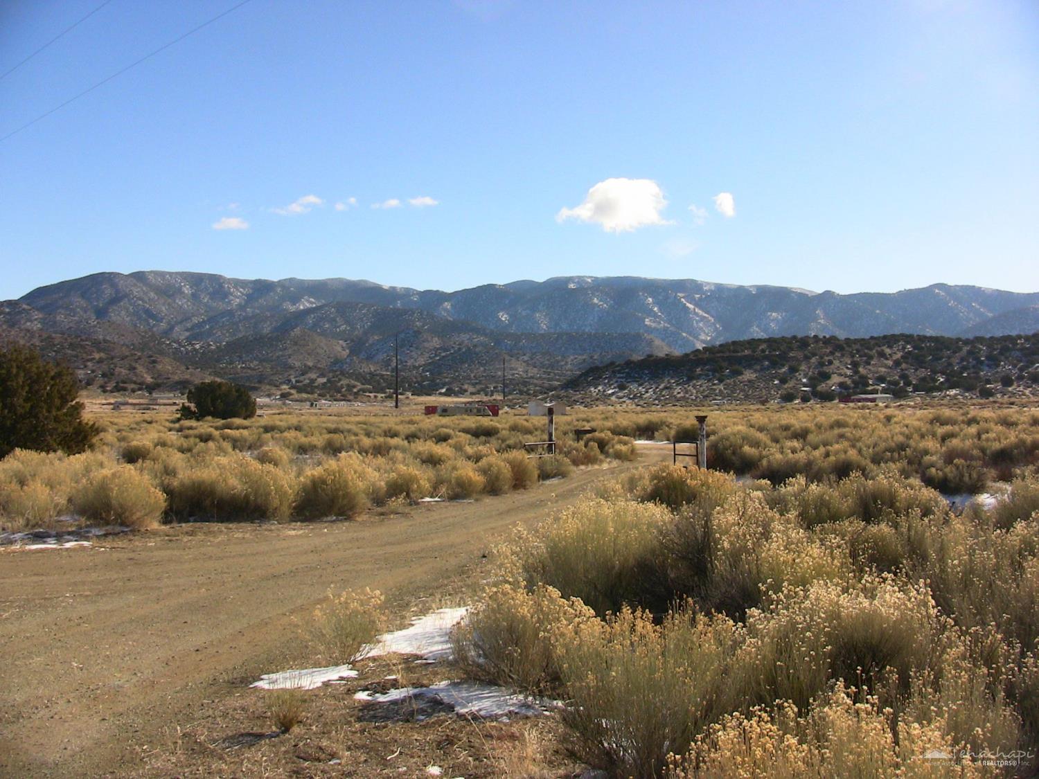 Open brush-covered lot with a dirt track, mountain views, and small patches of snow.