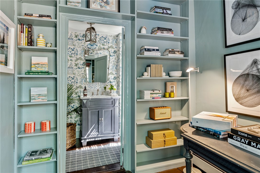 Study with built-in pale blue bookshelves, a dark desk, and a floral-wallpapered vanity alcove.
