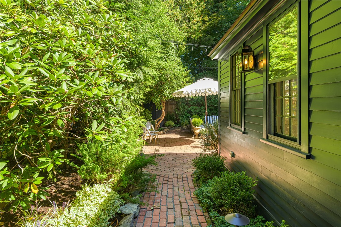 Brick garden patio beside a green-sided home, with a white umbrella and outdoor chairs.