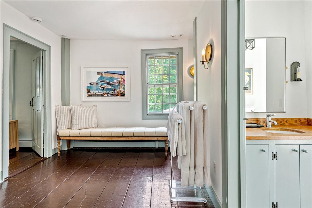 Bright bathroom with a wooden vanity, towel rack, and cushioned bench beneath a window.
