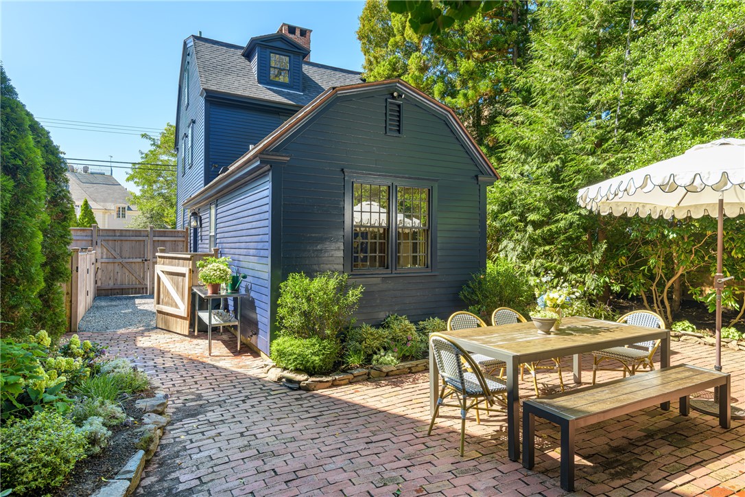 Dark blue house beside a brick patio furnished with an outdoor dining table and chairs.