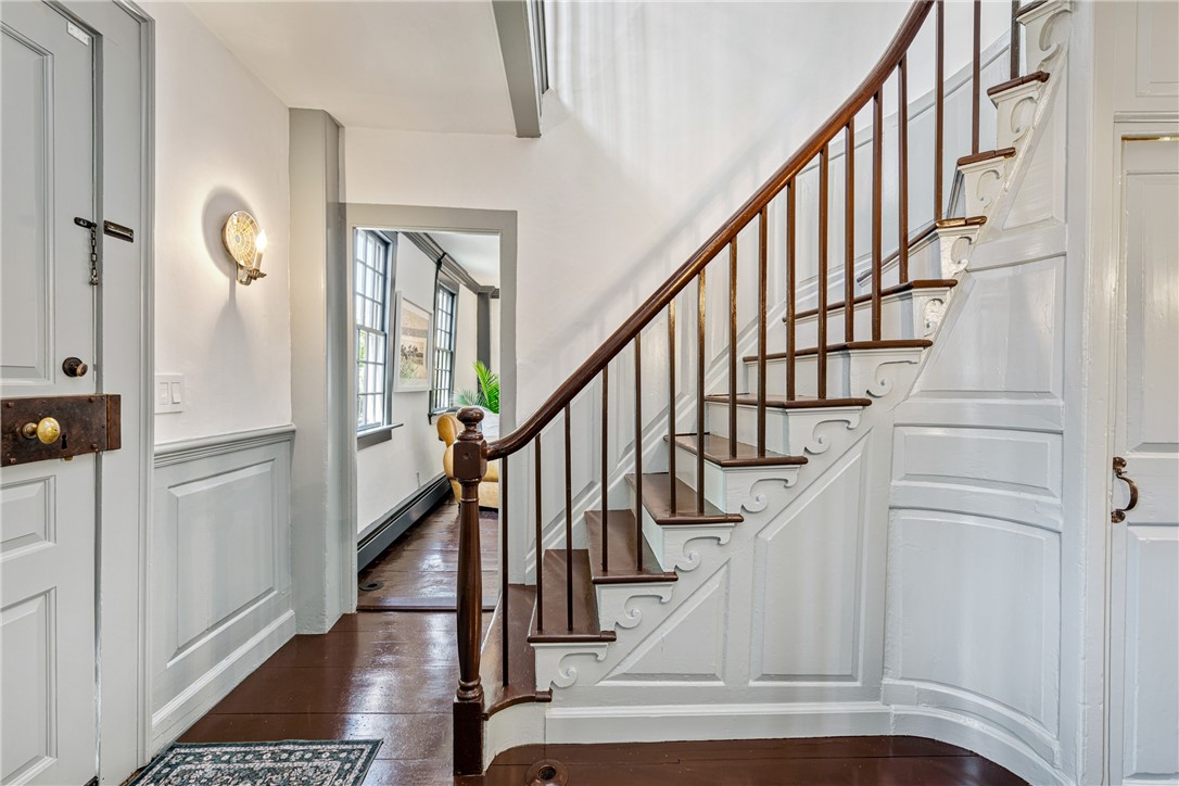 Entry hall with a curved wooden staircase, white paneled walls, and dark hardwood floors.