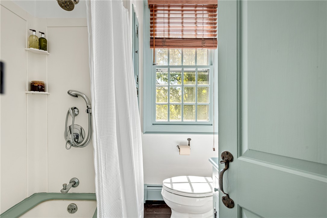 Bathroom with a bathtub, white shower curtain, and window with wooden blinds.