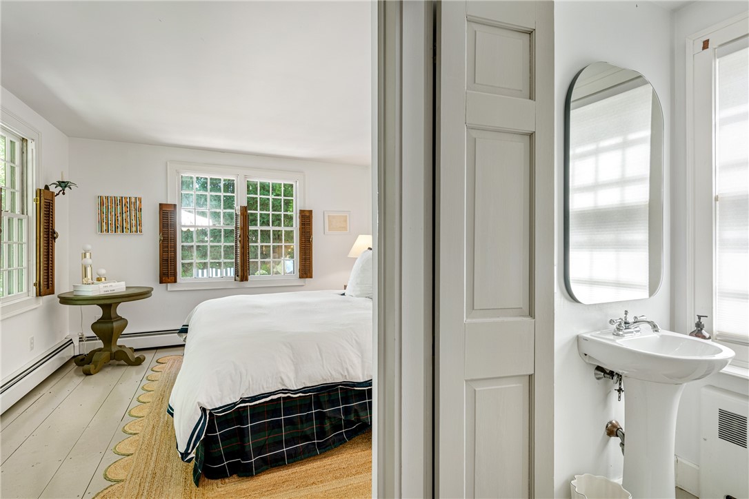 Bedroom with white bedding and shuttered windows beside a bathroom with a pedestal sink.