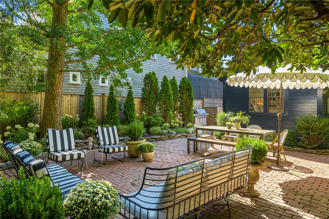 Brick courtyard patio with striped lounge chairs, a dining table, and leafy shade.