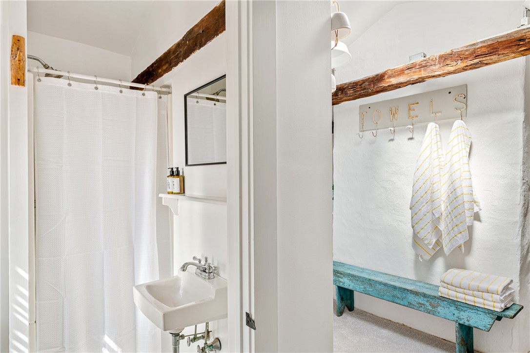 Bathroom with a white shower curtain, exposed wood beam, and turquoise towel bench.