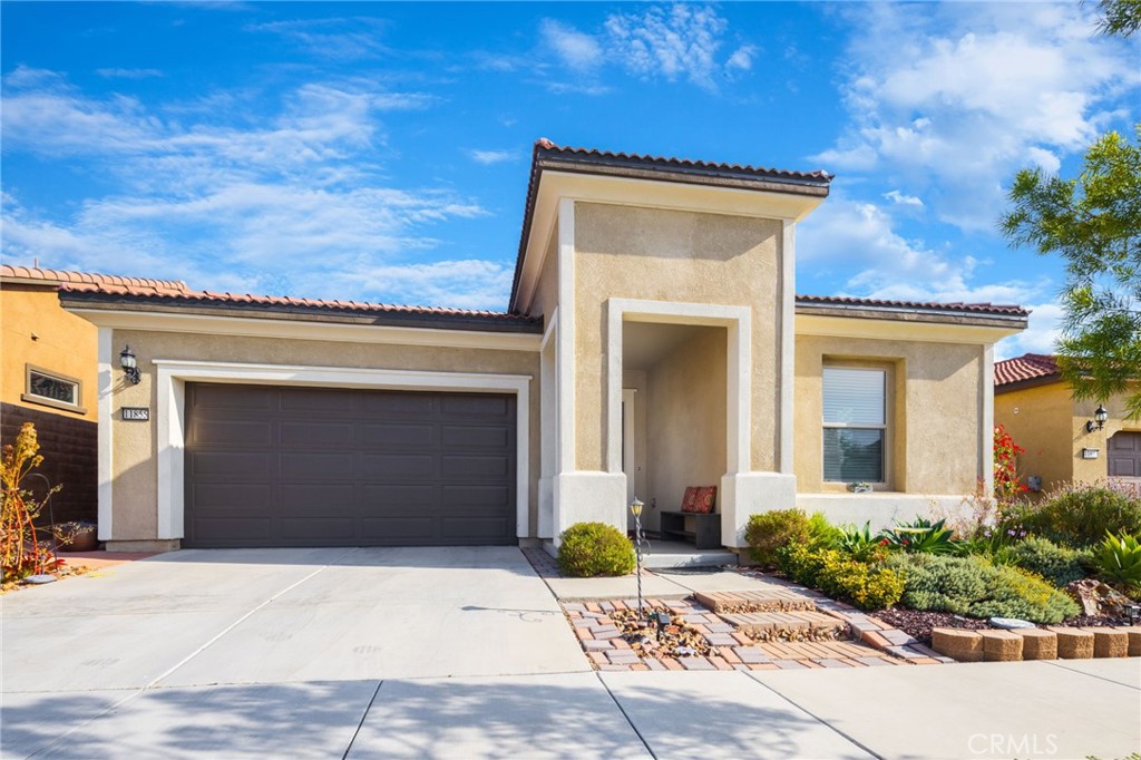 Stucco home with a recessed entry, dark double garage door, and landscaped front yard.
