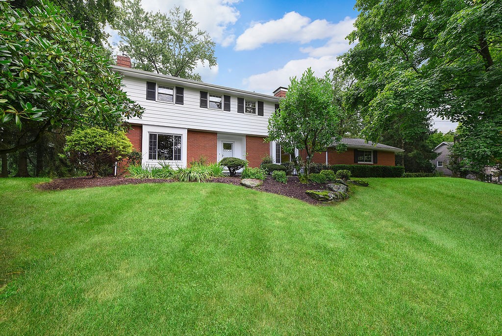 Two-story white-and-brick house with dark shutters, landscaped garden beds, and a broad green lawn.