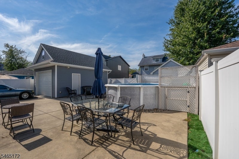 Backyard patio with outdoor dining set, closed umbrella, above-ground pool, and detached garage.