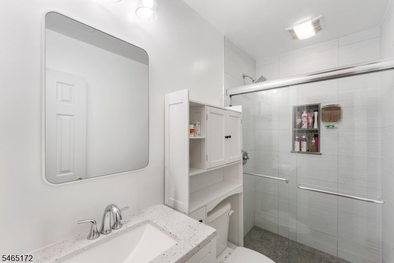 Bathroom with a white vanity and mirror beside a glass-enclosed tiled walk-in shower.