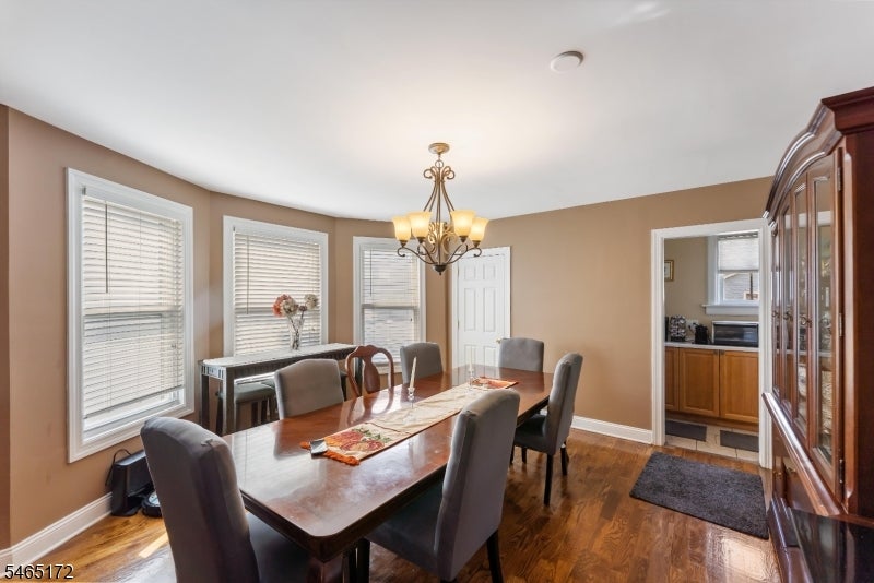 Dining room with a long wooden table, chandelier, hardwood floors, and windows with blinds.