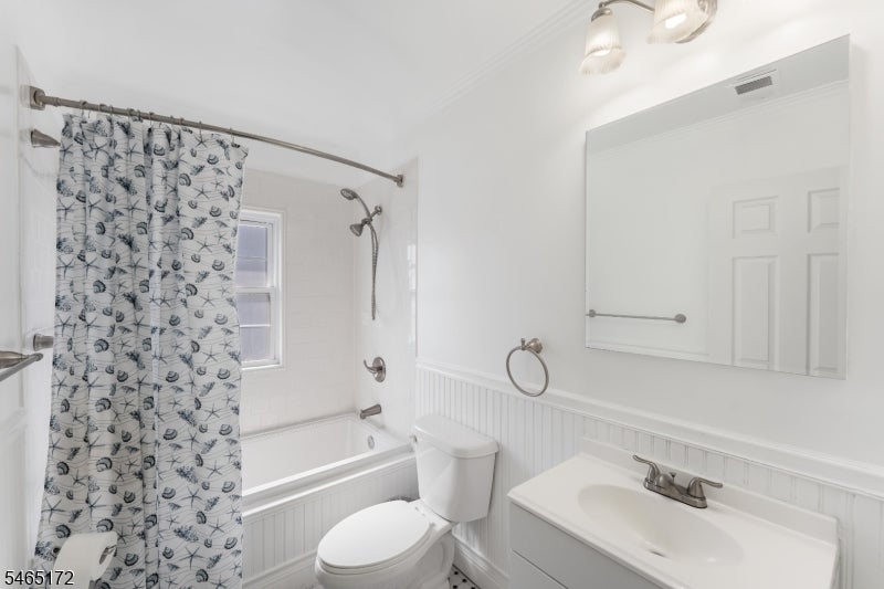 Bathroom with a patterned shower curtain, white bathtub, toilet, and vanity beneath a large mirrored cabinet.