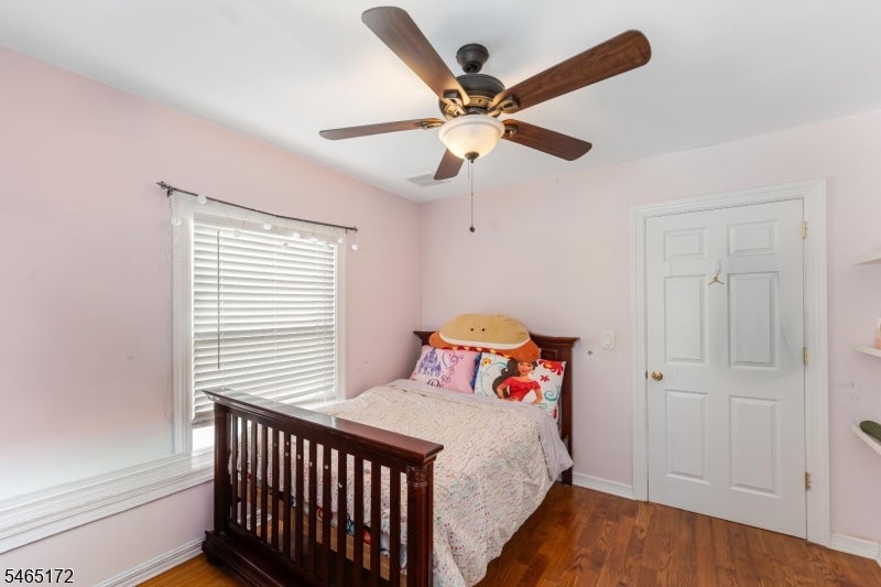 Bedroom with a dark wooden bed, pink walls, white blinds, and a ceiling fan.