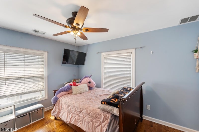 Bedroom with a pink quilted bed, plush toys, hardwood floors, and a ceiling fan.