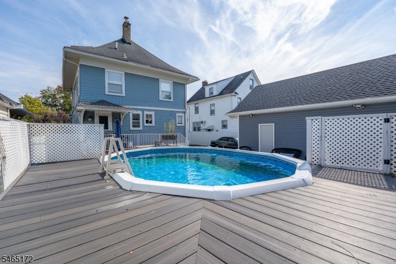 Above-ground pool on a spacious deck between a blue house and detached garage.