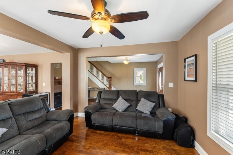 Furnished living room with dark reclining sofas, hardwood floors, and a ceiling fan.